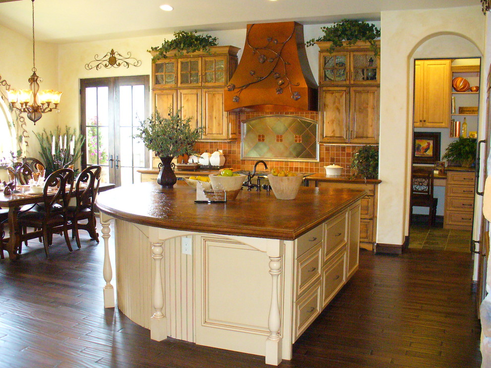 This is an example of a country l-shaped eat-in kitchen in Denver with raised-panel cabinets, beige cabinets, marble benchtops, orange splashback, mosaic tile splashback, panelled appliances, dark hardwood floors and with island.