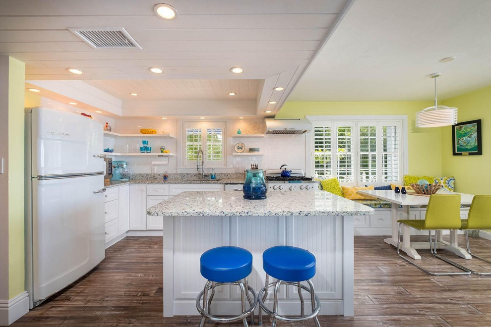 Inspiration for a mid-sized transitional u-shaped linoleum floor and brown floor eat-in kitchen remodel in Miami with an undermount sink, recessed-panel cabinets, white cabinets, granite countertops, white backsplash, subway tile backsplash, white appliances, an island and multicolored countertops