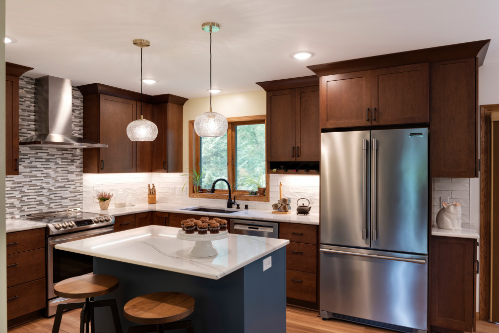 This is an example of a small transitional l-shaped open plan kitchen in Minneapolis with an undermount sink, shaker cabinets, dark wood cabinets, quartz benchtops, grey splashback, subway tile splashback, stainless steel appliances, medium hardwood floors, with island, brown floor and white benchtop.