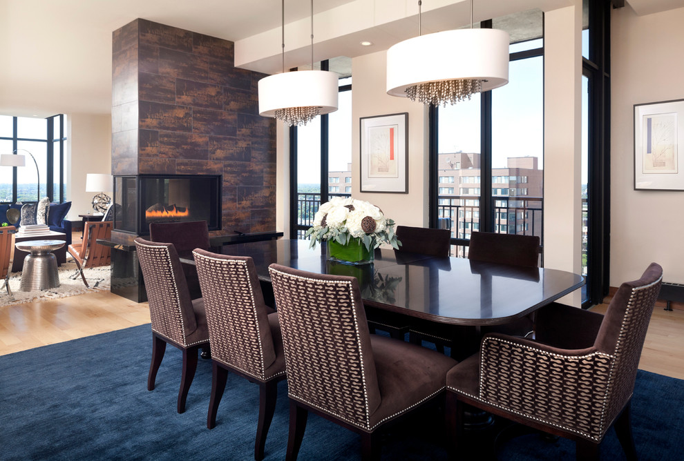 Design ideas for a contemporary open plan dining in Minneapolis with white walls, light hardwood floors, a two-sided fireplace and a plaster fireplace surround.
