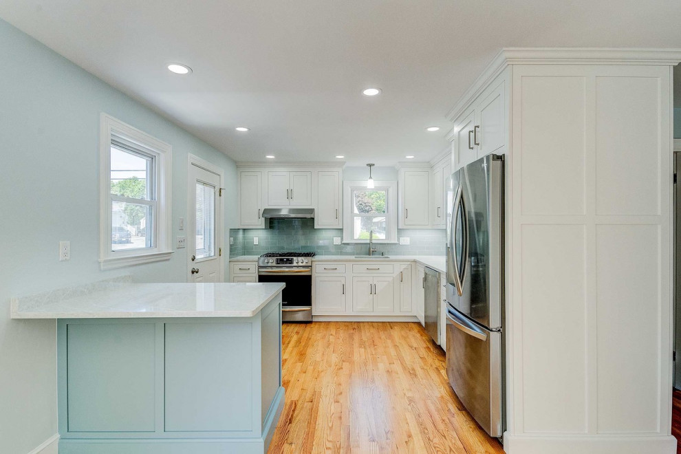 This is an example of a small beach style l-shaped eat-in kitchen in Boston with an undermount sink, shaker cabinets, white cabinets, quartzite benchtops, blue splashback, porcelain splashback, stainless steel appliances, medium hardwood floors, a peninsula, brown floor and white benchtop.