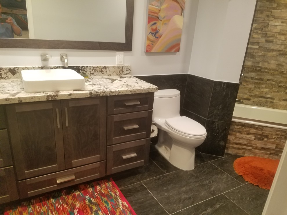Inspiration for a mid-sized transitional master bathroom in Miami with shaker cabinets, grey cabinets, an alcove tub, a shower/bathtub combo, a one-piece toilet, black tile, stone tile, grey walls, slate floors, a vessel sink, granite benchtops, black floor, a hinged shower door and white benchtops.