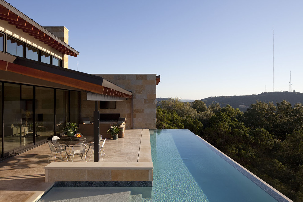 This is an example of a large contemporary backyard l-shaped infinity pool in Austin with tile and a hot tub.