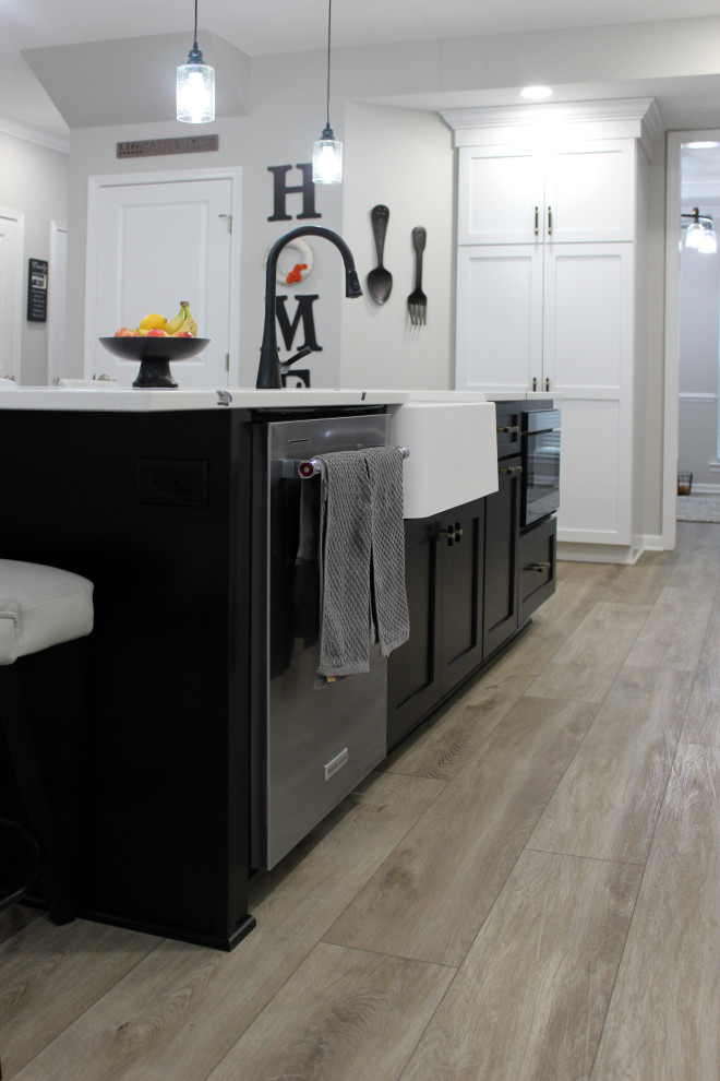 Example of a large transitional single-wall vinyl floor and beige floor eat-in kitchen design with a farmhouse sink, shaker cabinets, black cabinets, quartz countertops, black backsplash, subway tile backsplash, stainless steel appliances, an island and white countertops