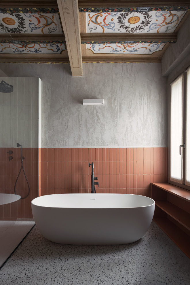 Cette image montre une salle de bain design avec une baignoire indépendante, une douche à l'italienne, un carrelage orange, un mur gris, un sol gris et poutres apparentes.