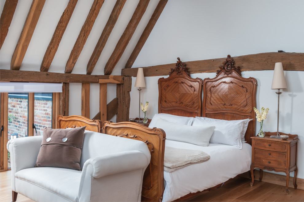 Mittelgroßes Country Gästezimmer mit weißer Wandfarbe, braunem Holzboden und freigelegten Dachbalken in Kent
