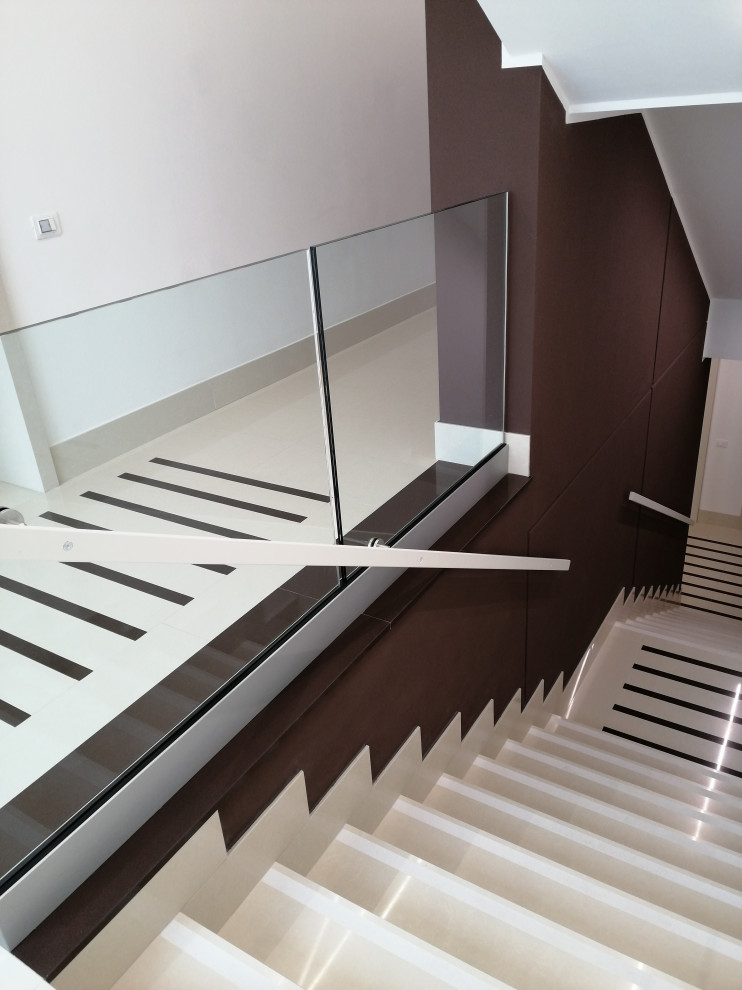 Réalisation d'un grand escalier droit minimaliste en marbre avec des contremarches en marbre et un garde-corps en verre.