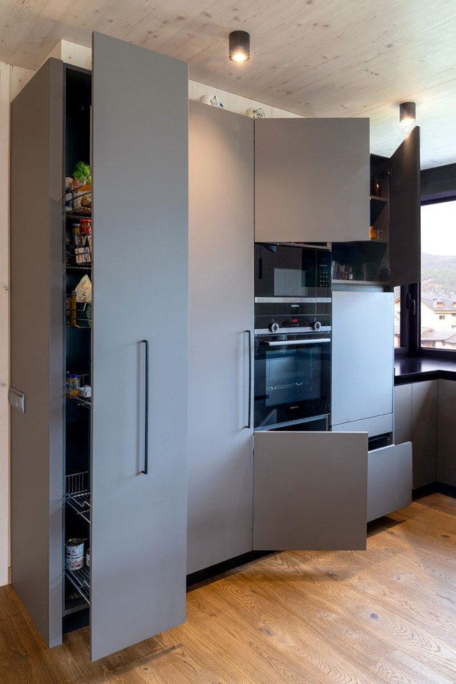 Modern inredning av ett kök, med släta luckor, grå skåp, mellanmörkt trägolv, en halv köksö och brunt golv