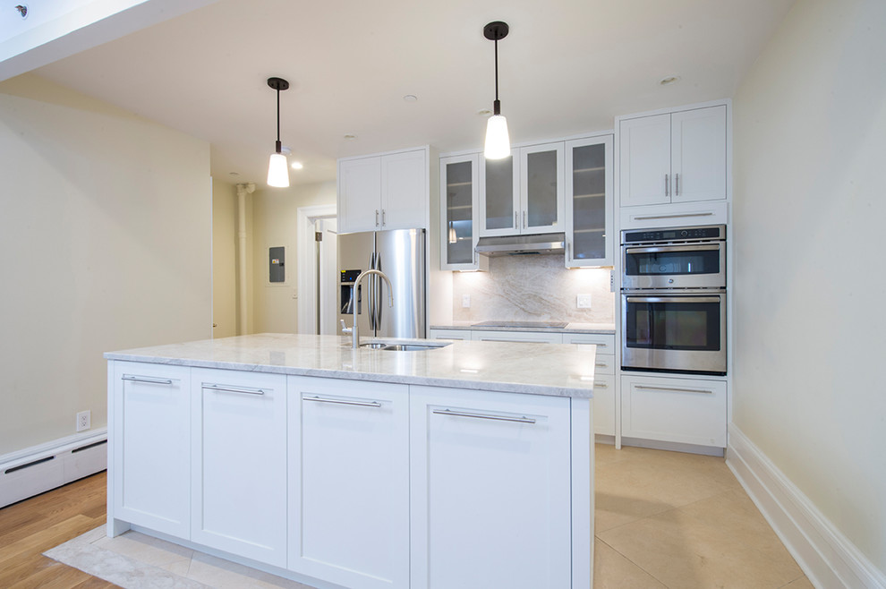 Photo of a large traditional kitchen in New York with a double-bowl sink, recessed-panel cabinets, white cabinets, marble benchtops, beige splashback, marble splashback, stainless steel appliances, ceramic floors, with island, beige floor and beige benchtop.