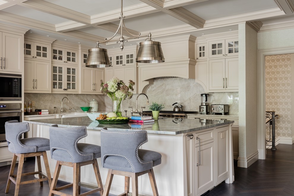 Photo of a traditional l-shaped kitchen in Boston with a farmhouse sink, shaker cabinets, beige cabinets, beige splashback, stone slab splashback, stainless steel appliances, dark hardwood floors, with island, brown floor and grey benchtop.