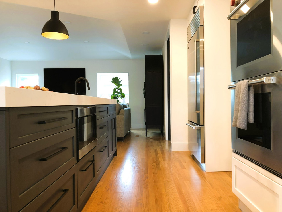 This is an example of a medium sized traditional l-shaped open plan kitchen in San Francisco with a single-bowl sink, shaker cabinets, black cabinets, engineered stone countertops, white splashback, ceramic splashback, stainless steel appliances, medium hardwood flooring, an island and white worktops.