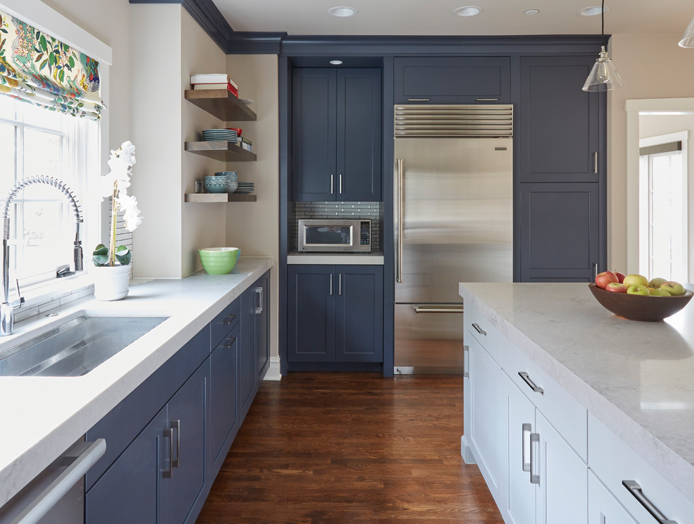 Inspiration for a mid-sized transitional u-shaped dark wood floor and brown floor kitchen remodel with an undermount sink, recessed-panel cabinets, blue cabinets, white backsplash, ceramic backsplash, stainless steel appliances, an island and white countertops