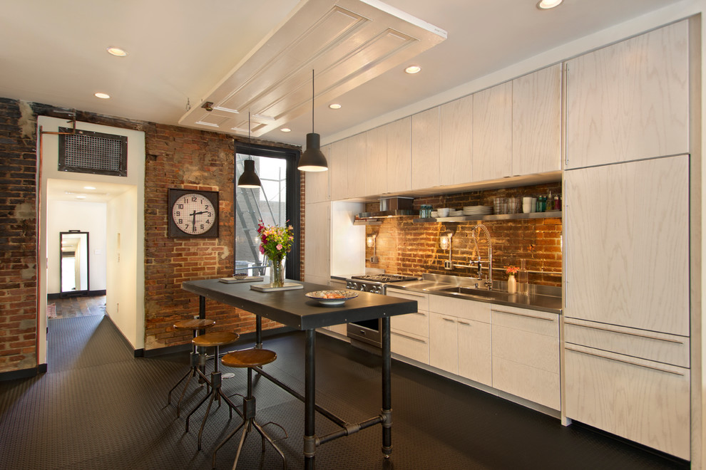 This is an example of an industrial single-wall kitchen in DC Metro with flat-panel cabinets, light wood cabinets, stainless steel benchtops, with island, an integrated sink, stainless steel appliances and brown splashback.