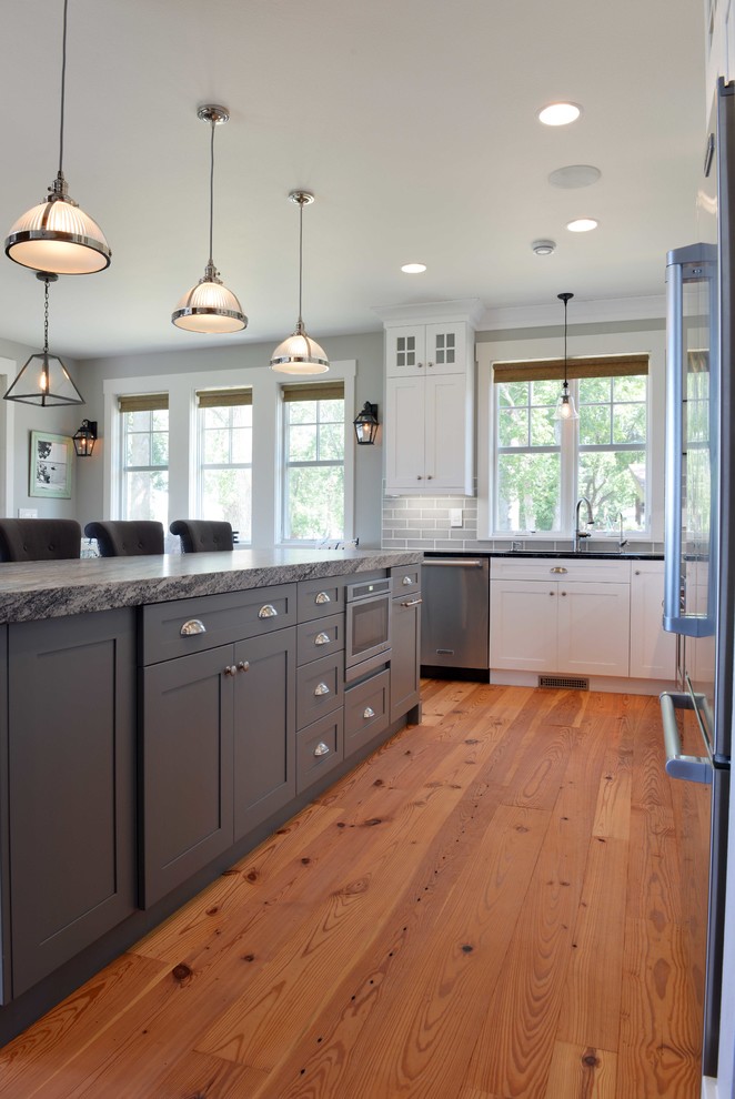 Mid-sized transitional l-shaped light wood floor eat-in kitchen photo with shaker cabinets, white cabinets, granite countertops, gray backsplash, subway tile backsplash, stainless steel appliances, an island and an undermount sink