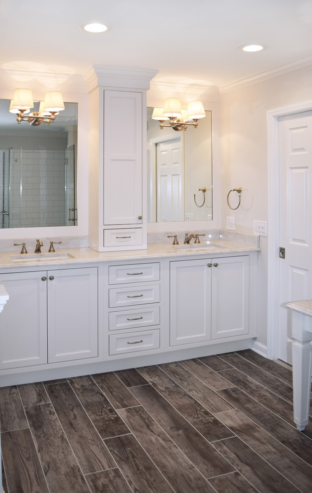 This is an example of a large traditional master bathroom in Philadelphia with shaker cabinets, white cabinets, a freestanding tub, a one-piece toilet, gray tile, subway tile, grey walls, porcelain floors, an undermount sink, marble benchtops, brown floor and a hinged shower door.