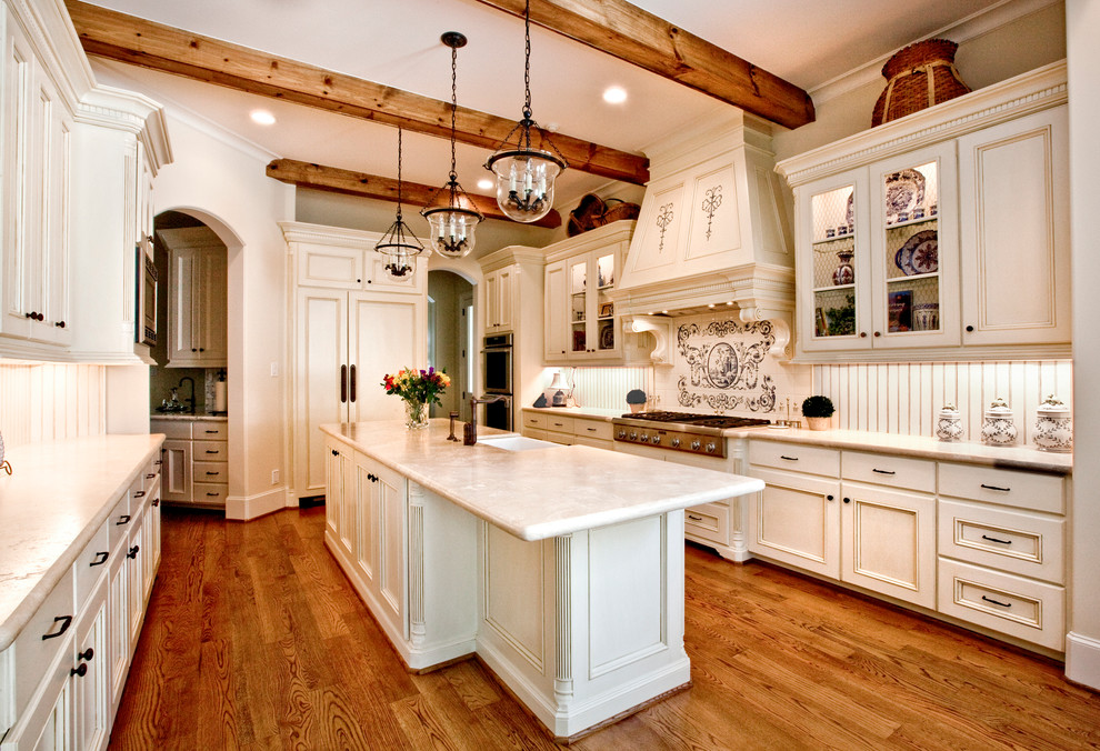 This is an example of a mid-sized traditional u-shaped separate kitchen in Houston with a farmhouse sink, recessed-panel cabinets, beige cabinets, beige splashback, panelled appliances, medium hardwood floors, with island, quartzite benchtops, timber splashback and brown floor.