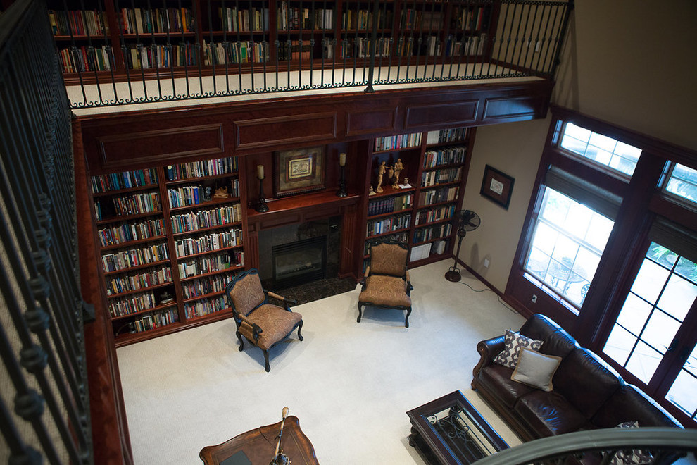 Expansive traditional home office in Other with a library, brown walls, carpet, a standard fireplace, a tile fireplace surround, a freestanding desk and grey floor.