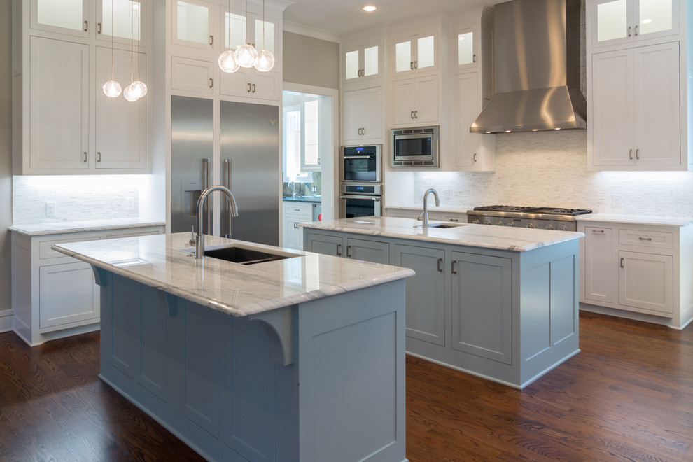 Example of a large transitional l-shaped dark wood floor and brown floor open concept kitchen design in Dallas with an undermount sink, recessed-panel cabinets, white cabinets, marble countertops, white backsplash, stone tile backsplash, stainless steel appliances, two islands and white countertops