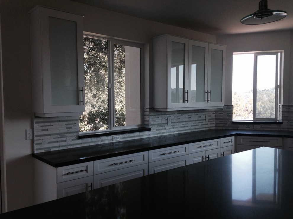 Inspiration for a mid-sized transitional l-shaped travertine floor eat-in kitchen remodel in Los Angeles with white cabinets, solid surface countertops, multicolored backsplash, stainless steel appliances, an island, marble backsplash and recessed-panel cabinets
