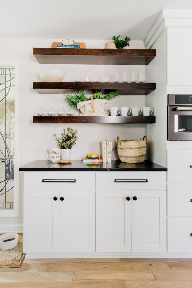 Design ideas for a modern galley eat-in kitchen in Omaha with a farmhouse sink, raised-panel cabinets, white cabinets, quartz benchtops, beige splashback, ceramic splashback, black appliances, with island and black benchtop.