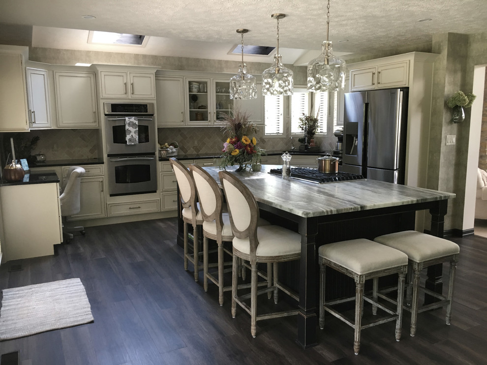 Large transitional u-shaped laminate floor and gray floor eat-in kitchen photo with an undermount sink, recessed-panel cabinets, white cabinets, granite countertops, white backsplash, ceramic backsplash, stainless steel appliances, an island and black countertops