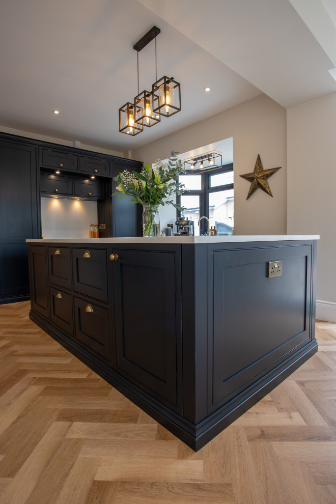This is an example of a medium sized classic cream and black kitchen/diner in Essex with shaker cabinets, black cabinets, quartz worktops, white splashback, medium hardwood flooring, an island, brown floors, white worktops and a feature wall.