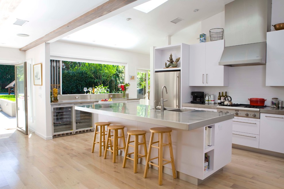 Inspiration for a contemporary galley open plan kitchen in Los Angeles with flat-panel cabinets, white cabinets, stainless steel benchtops, stainless steel appliances and an integrated sink.