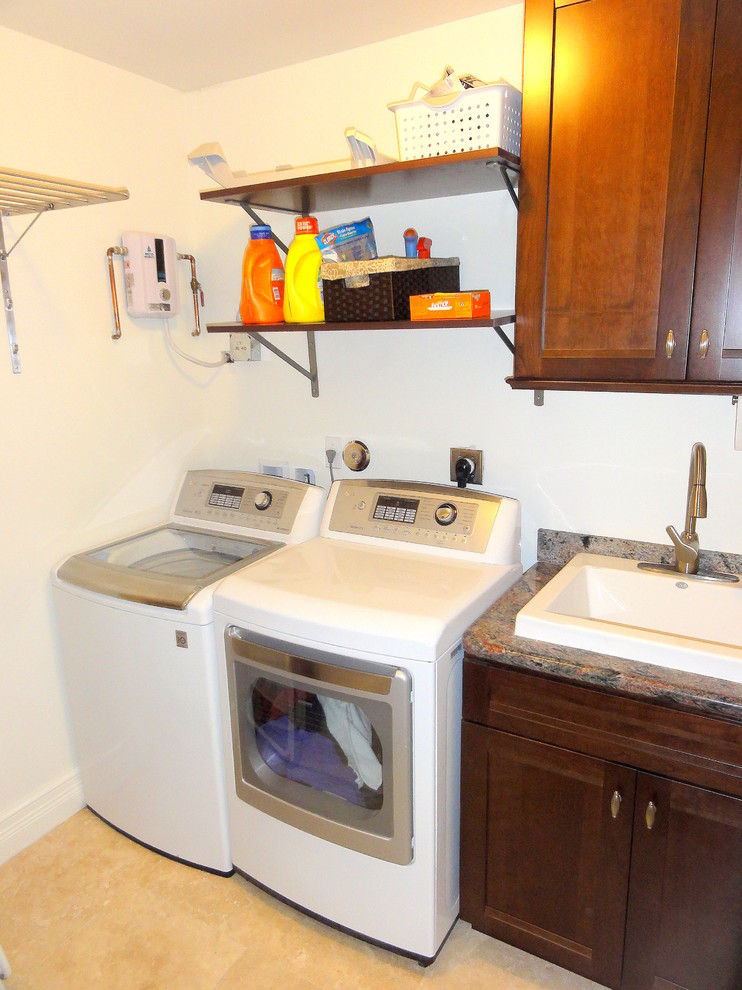 This is an example of a small transitional single-wall dedicated laundry room in Miami with recessed-panel cabinets, dark wood cabinets, granite benchtops, white walls, travertine floors, a side-by-side washer and dryer and a drop-in sink.