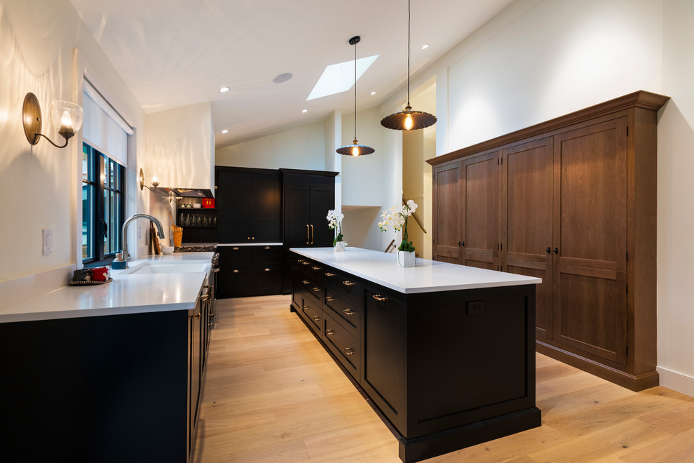 Inspiration for a mid-sized rustic l-shaped light wood floor and beige floor open concept kitchen remodel in Vancouver with a farmhouse sink, shaker cabinets, black cabinets, quartz countertops, paneled appliances, an island and white countertops