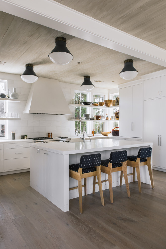 Photo of a beach style l-shaped kitchen in Charleston with white cabinets, white splashback, panelled appliances, light hardwood floors and with island.