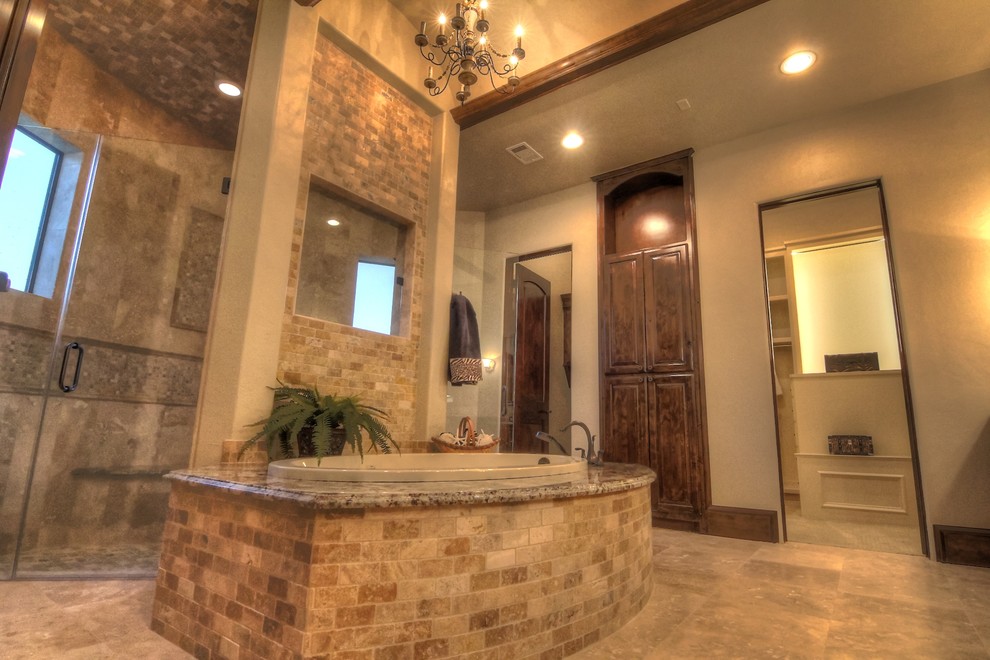 This is an example of a large mediterranean master bathroom in Houston with raised-panel cabinets, dark wood cabinets, a drop-in tub, an alcove shower, a two-piece toilet, beige tile, stone tile, beige walls, limestone floors, an undermount sink and granite benchtops.