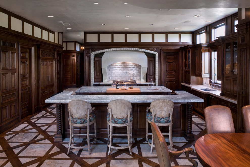 This is an example of a traditional eat-in kitchen in Austin with a single-bowl sink, raised-panel cabinets, dark wood cabinets, limestone benchtops and panelled appliances.