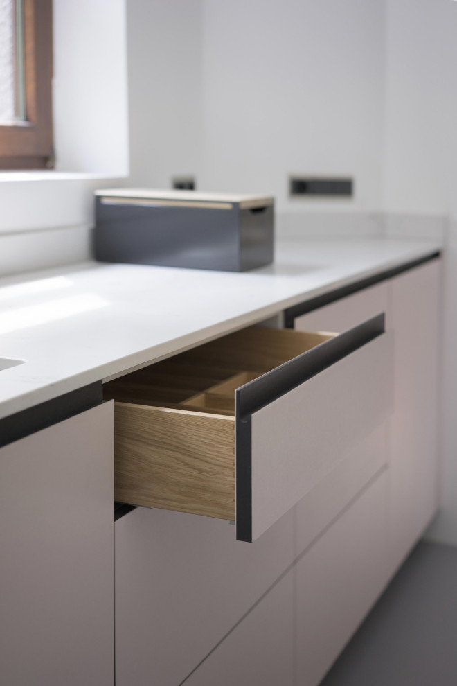Large modern galley eat-in kitchen in Berlin with a drop-in sink, flat-panel cabinets, pink cabinets, quartz benchtops, white splashback, window splashback, panelled appliances, linoleum floors, with island, grey floor and white benchtop.