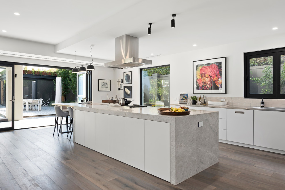 Large modern single-wall open plan kitchen in Melbourne with a double-bowl sink, recessed-panel cabinets, white cabinets, marble benchtops, beige splashback, ceramic splashback, stainless steel appliances, light hardwood floors, with island, grey floor and multi-coloured benchtop.