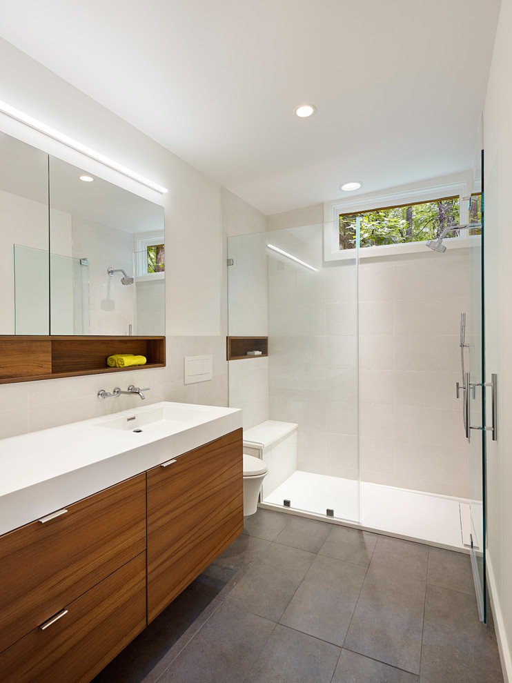 This is an example of a small modern master bathroom in Baltimore with flat-panel cabinets, brown cabinets, a curbless shower, a wall-mount toilet, yellow tile, porcelain tile, white walls, porcelain floors, an integrated sink, solid surface benchtops, grey floor and a hinged shower door.
