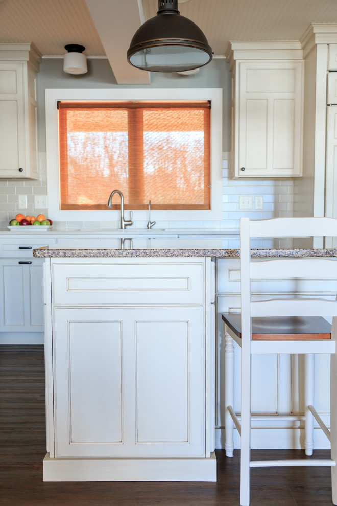 Example of a transitional l-shaped vinyl floor open concept kitchen design in Nashville with an undermount sink, raised-panel cabinets, white cabinets, quartz countertops, beige backsplash, ceramic backsplash, paneled appliances and an island