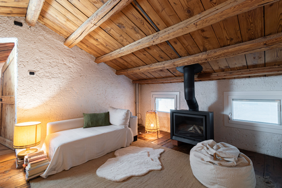 На фото: открытая гостиная комната среднего размера в стиле рустика с белыми стенами, деревянным полом, оранжевым полом, балками на потолке и печью-буржуйкой