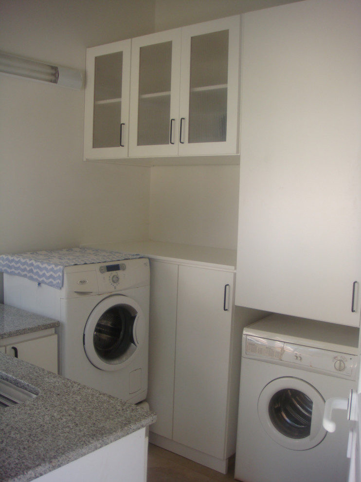 Idéer för att renovera en stor funkis grå u-formad grått tvättstuga enbart för tvätt och med garderob, med släta luckor, vita skåp, granitbänkskiva, vita väggar, klinkergolv i keramik och beiget golv