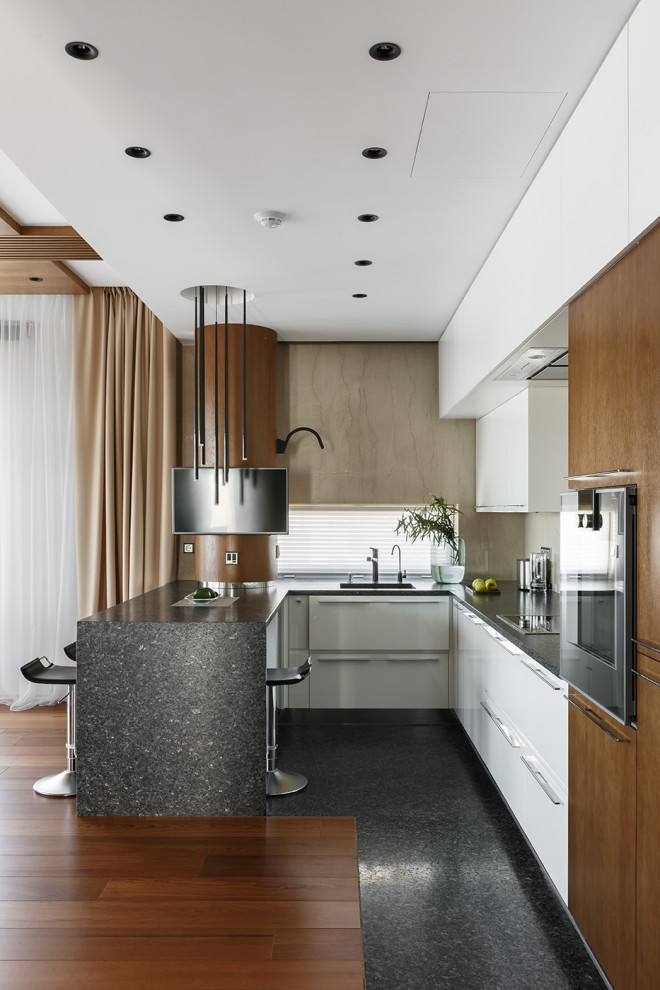 This is an example of a large contemporary u-shaped kitchen/diner in Saint Petersburg with a submerged sink, flat-panel cabinets, medium wood cabinets, granite worktops, beige splashback, marble splashback, black appliances, a breakfast bar, grey floors, grey worktops and a wood ceiling.