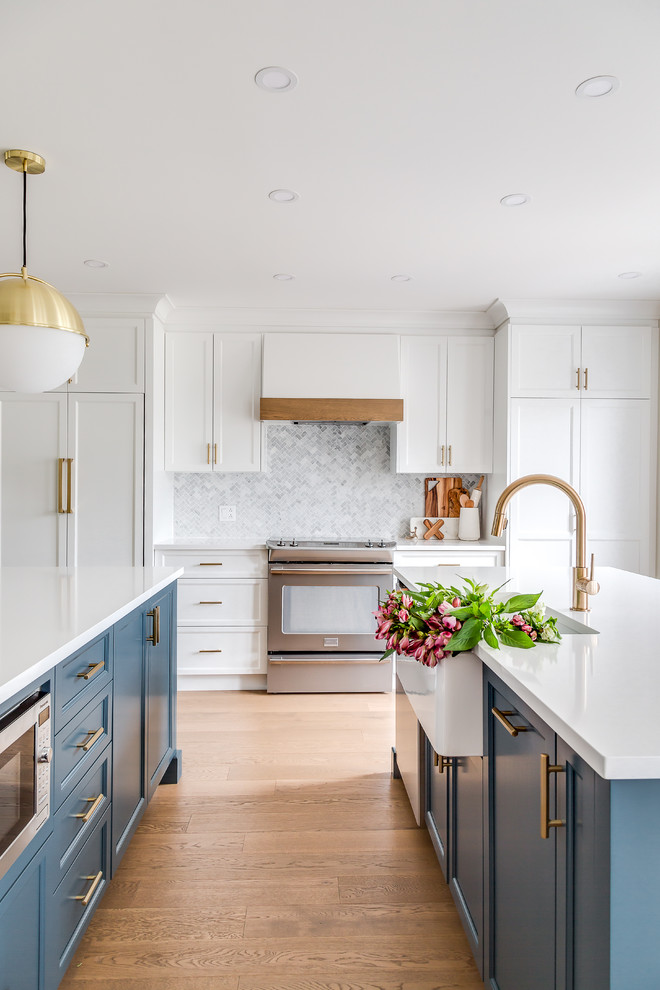 Inspiration for a large contemporary u-shaped open plan kitchen in Montreal with a farmhouse sink, shaker cabinets, blue cabinets, quartz benchtops, white splashback, marble splashback, panelled appliances, medium hardwood floors, multiple islands and brown floor.