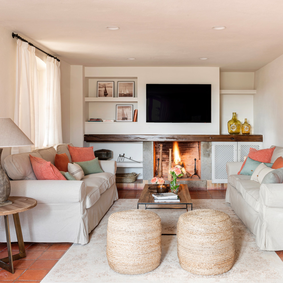 Immagine di un soggiorno mediterraneo con pareti bianche, pavimento in terracotta, camino classico, TV a parete e pavimento rosso