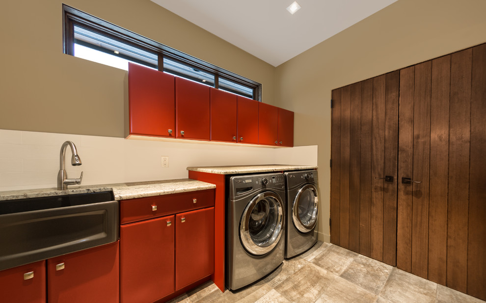 This is an example of a large country utility room in Vancouver with a farmhouse sink, flat-panel cabinets, red cabinets, granite benchtops, beige walls, porcelain floors and a side-by-side washer and dryer.