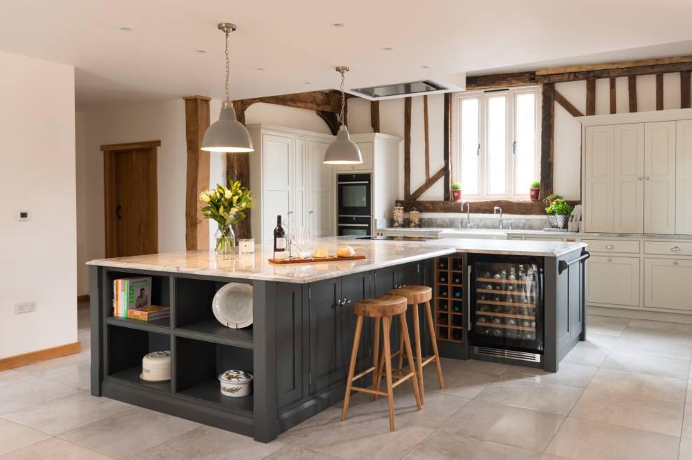 This is an example of an expansive country single-wall open plan kitchen in Essex with a farmhouse sink, shaker cabinets, medium wood cabinets, quartzite benchtops, white splashback, engineered quartz splashback, black appliances, ceramic floors, with island, grey floor, white benchtop and exposed beam.