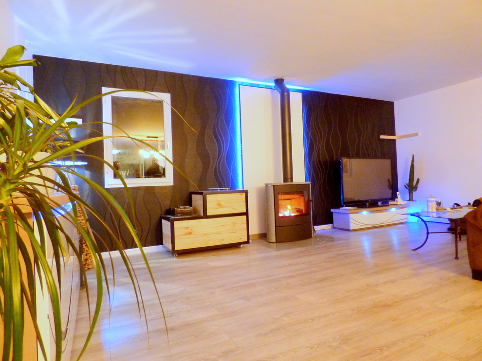Modelo de salón abierto minimalista grande con paredes negras, suelo laminado, estufa de leña, televisor independiente y suelo gris