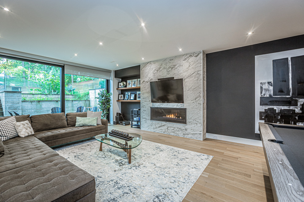 Large contemporary look-out basement in Toronto with a game room, black walls, medium hardwood floors, a ribbon fireplace and beige floor.