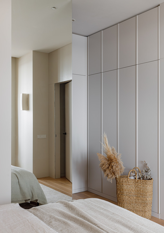 Exemple d'une armoire encastrée tendance de taille moyenne avec un placard avec porte à panneau surélevé, des portes de placard beiges, parquet clair et un sol blanc.