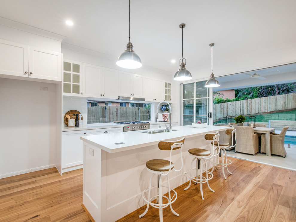Inspiration for a mid-sized traditional eat-in kitchen in Brisbane with an undermount sink, shaker cabinets, white cabinets, quartzite benchtops, white splashback, ceramic splashback, stainless steel appliances, light hardwood floors, with island and white benchtop.