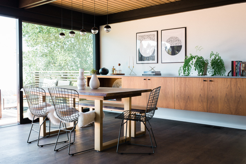 This is an example of a midcentury dining room in San Francisco with white walls, dark hardwood floors, no fireplace and brown floor.