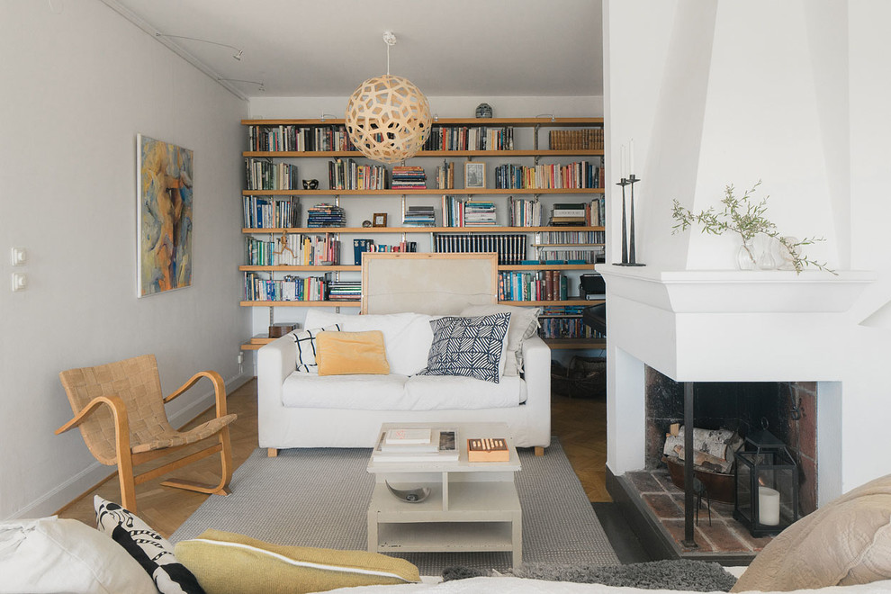 This is an example of a scandinavian open concept living room in Stockholm with a library, white walls, light hardwood floors, a plaster fireplace surround, no tv and a two-sided fireplace.