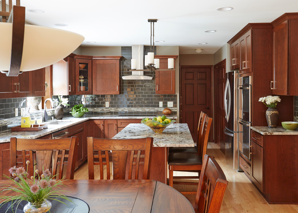 Inspiration for a large transitional l-shaped light wood floor home design remodel in Milwaukee with an undermount sink, shaker cabinets, dark wood cabinets, granite countertops, gray backsplash, subway tile backsplash, stainless steel appliances and an island